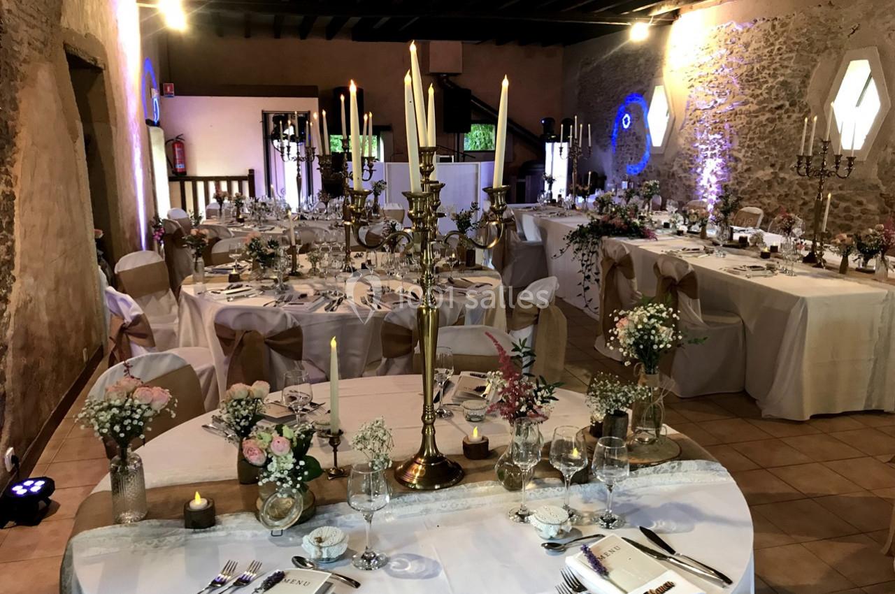 Salle de réception décorée pour un mariage avec tables rondes et rectangulaires ornées de chandeliers et fleurs.