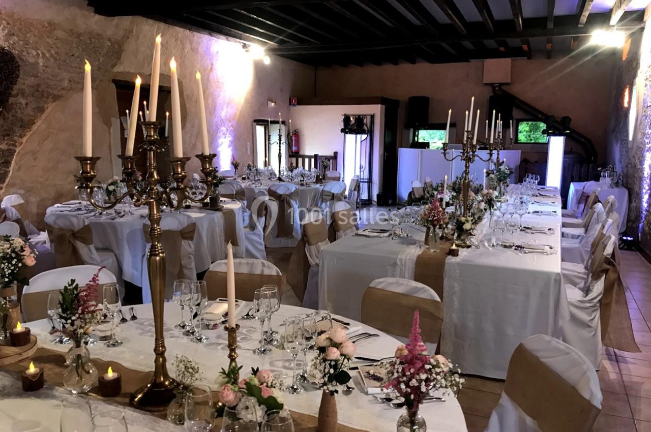 Salle de réception décorée avec des tables dressées, chandeliers dorés, fleurs et éclairage tamisé.