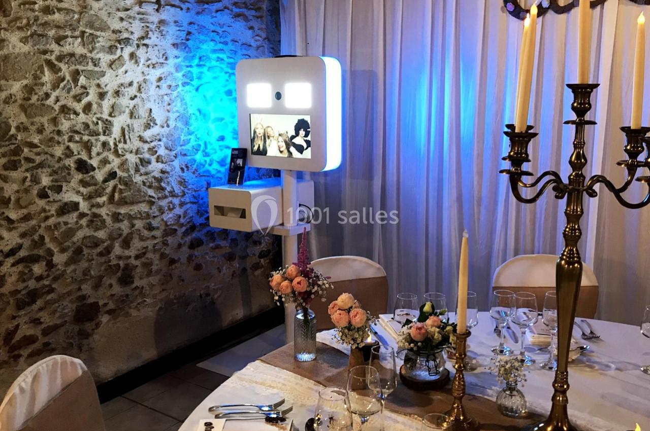 Borne photo lumineuse installée dans une salle de réception, entourée de décorations florales et d'une table dressée.