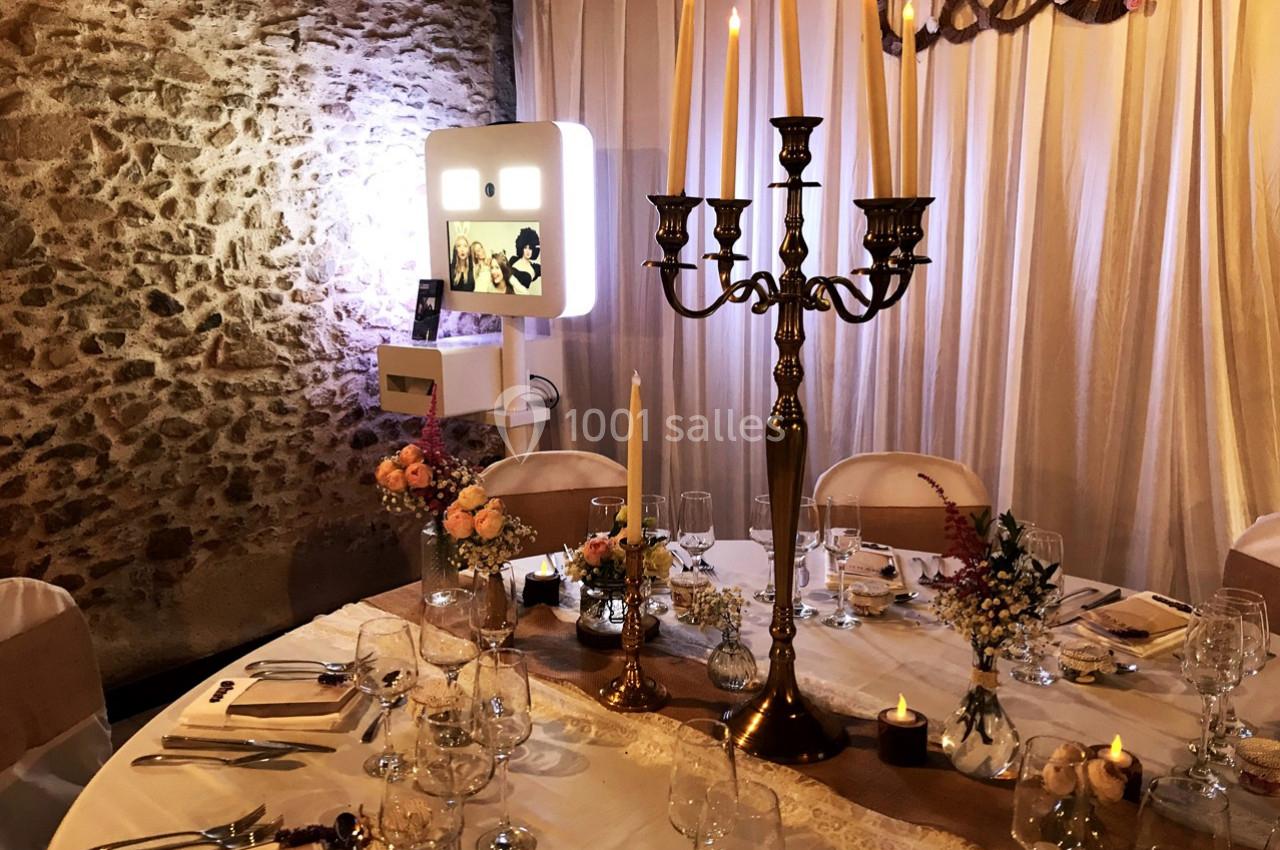 Table de réception décorée avec des chandeliers, fleurs et bougies, dans une salle aux murs en pierre et rideaux clairs.