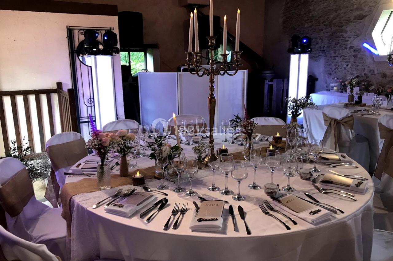 Table de réception élégamment dressée avec nappes blanches, chandeliers, fleurs et vaisselle raffinée dans une salle décorée.