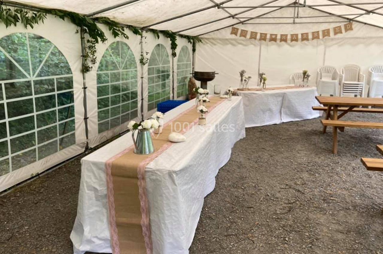 Intérieur d'une tente décorée pour un événement, avec tables recouvertes de nappes blanches et ornées de fleurs.