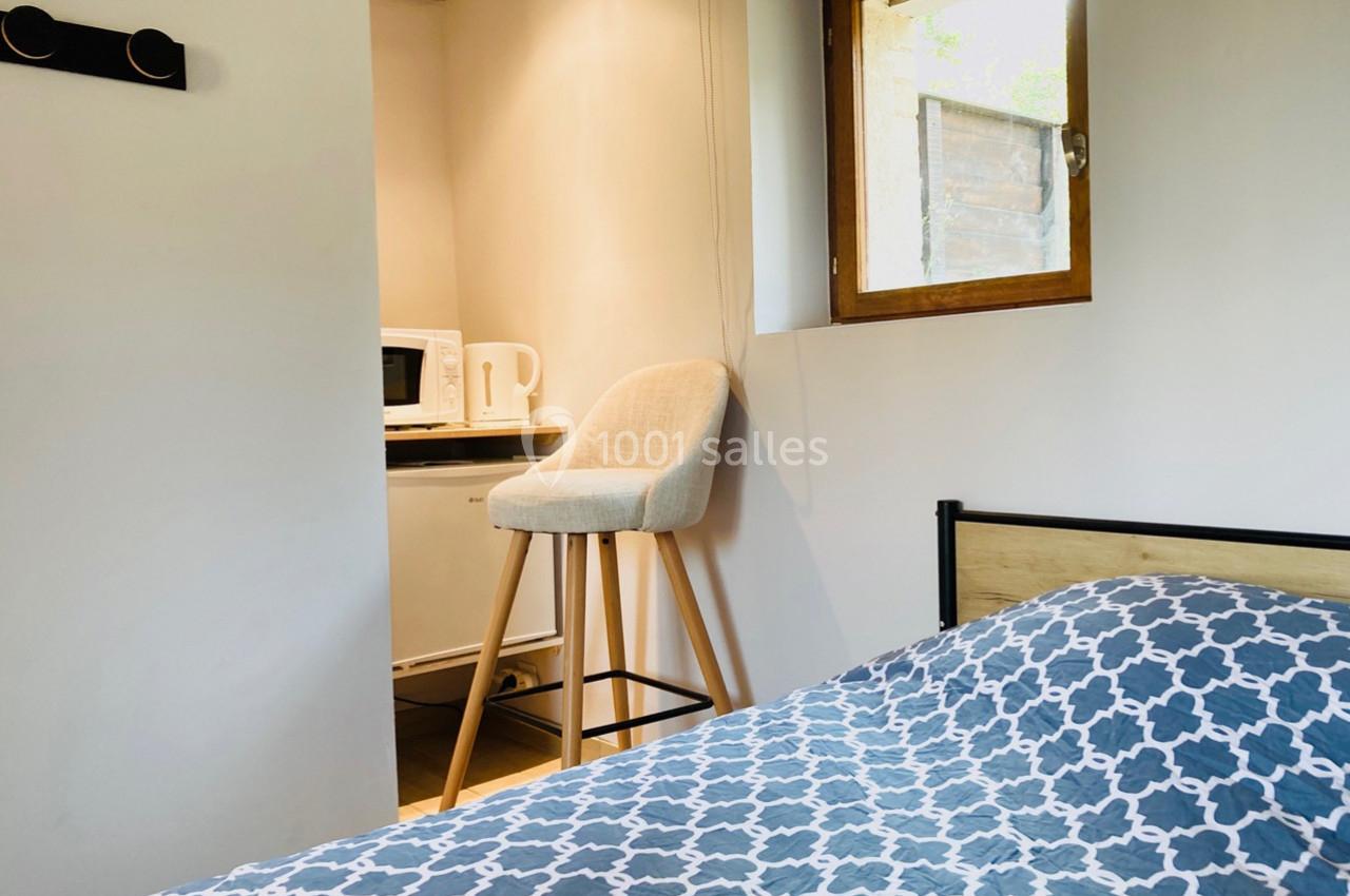 Vue d'une chambre avec un lit, une chaise haute près d'une fenêtre et un coin kitchenette équipé d'un micro-ondes.