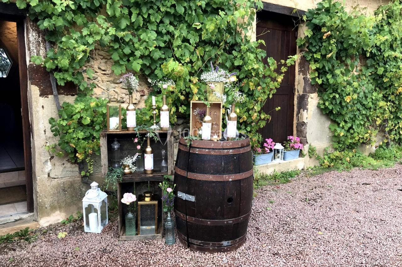 Décoration rustique avec tonneau, caisses en bois, bouteilles fleuries et lanternes devant un mur couvert de vigne.