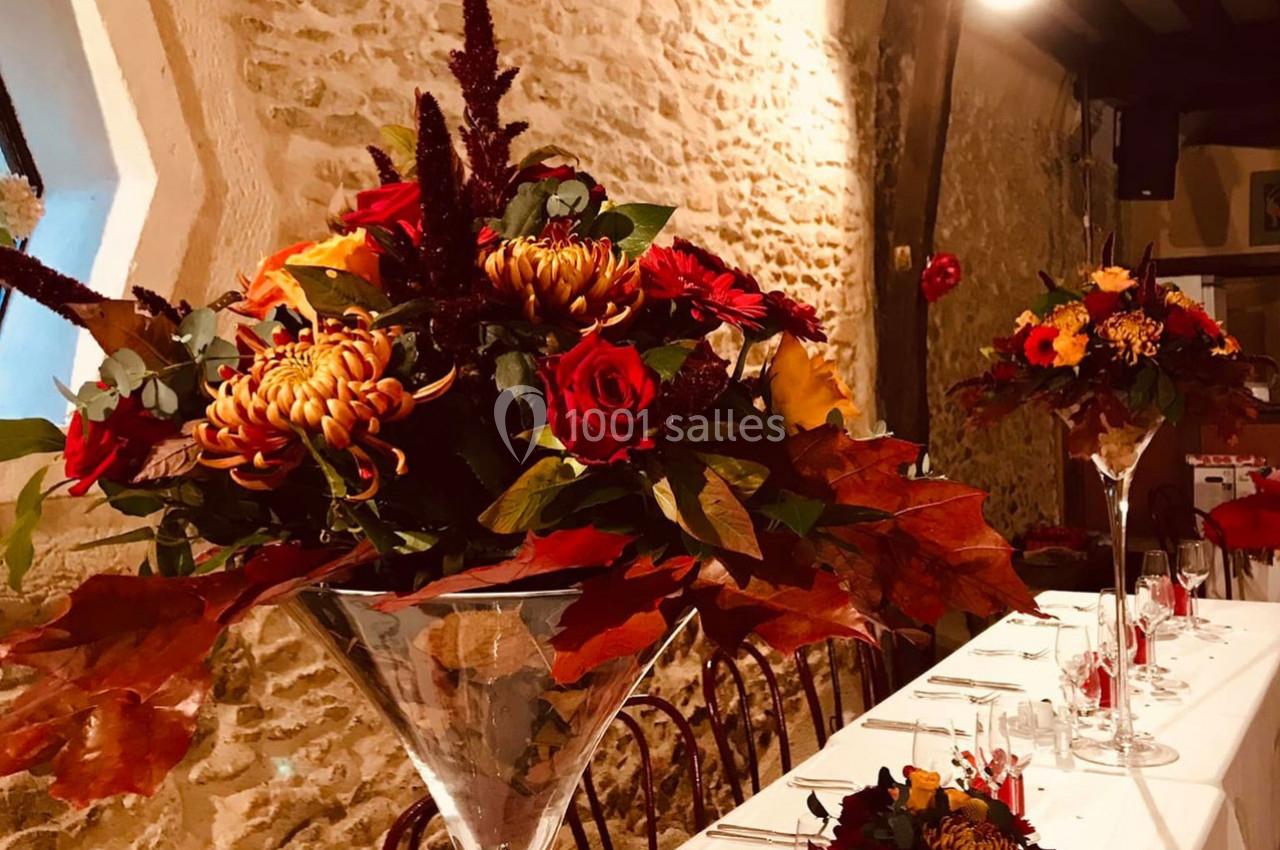 Bouquets de fleurs automnales avec des roses et des feuilles rouges décorant une table dans une salle en pierre.