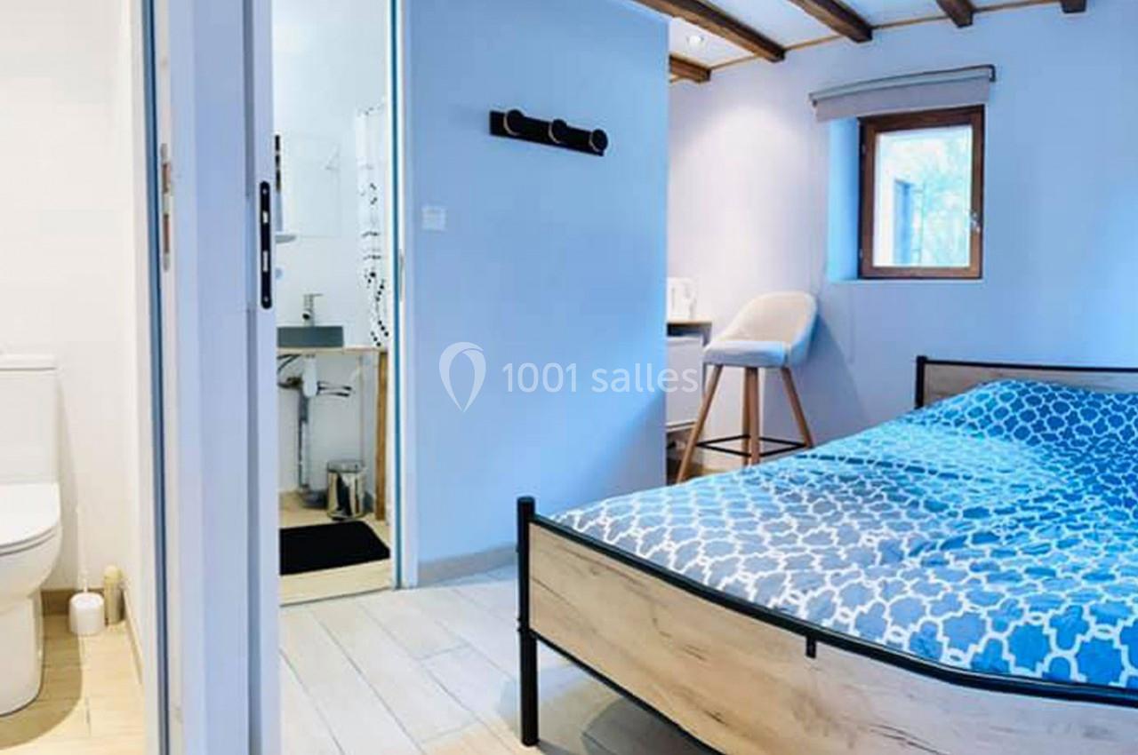 Chambre lumineuse avec lit double, salle de bain attenante, murs bleus et mobilier moderne.