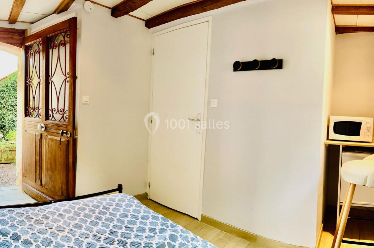 Chambre lumineuse avec lit, porte en bois, mur blanc, micro-ondes sur un meuble et porte-manteaux mural.