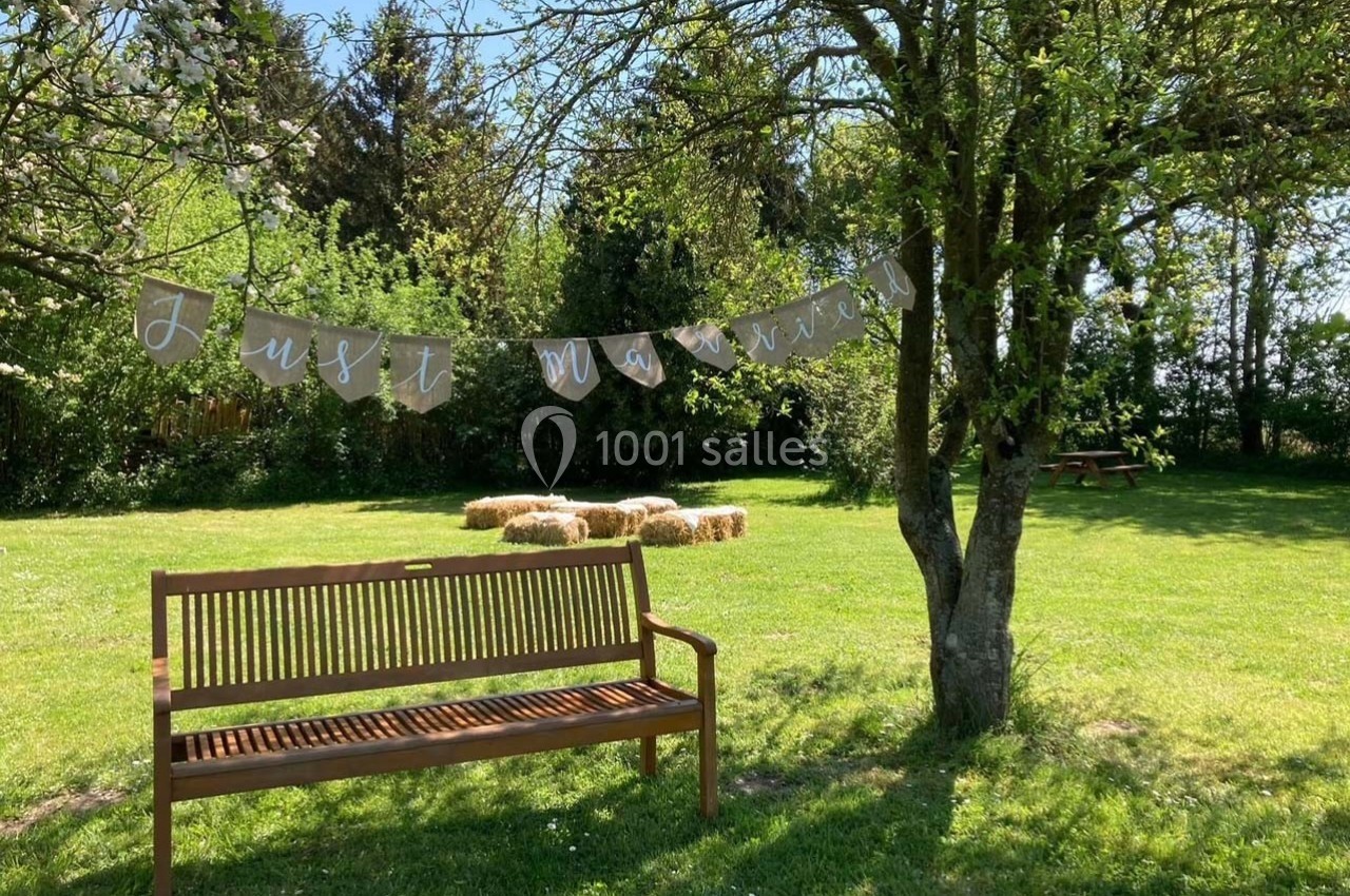 Banc en bois sous un arbre avec une guirlande ’Just Married’ et des bottes de foin dans un jardin verdoyant.