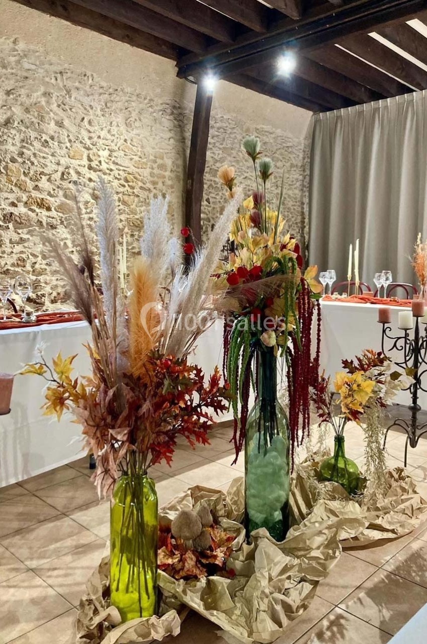 Décoration florale automnale avec pampas, feuillages et fleurs colorées dans des vases en verre, sur un sol en papier kraft.