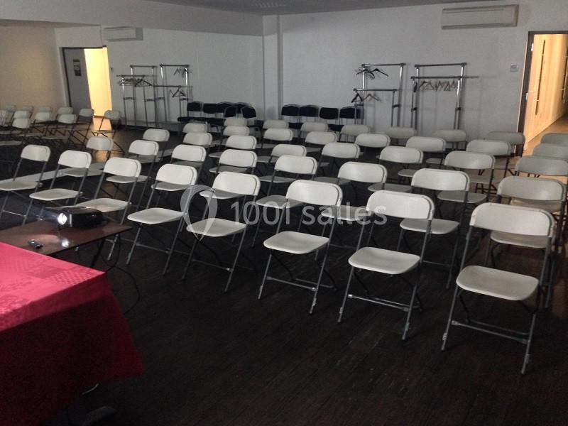Salle vide avec des rangées de chaises pliantes blanches alignées devant un projecteur sur une table.