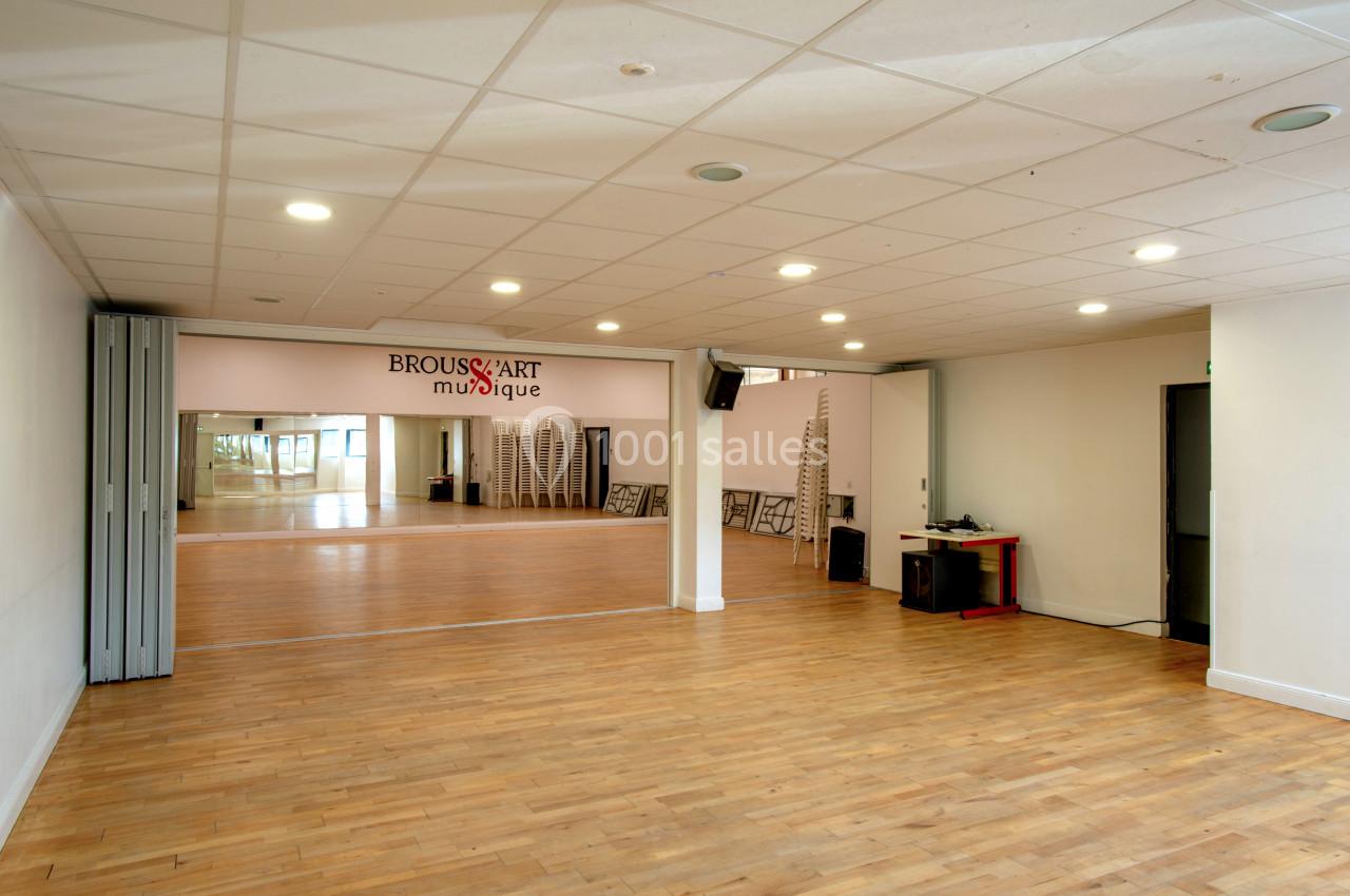 Salle spacieuse avec parquet, miroirs muraux, chaises empilées et éclairage au plafond.