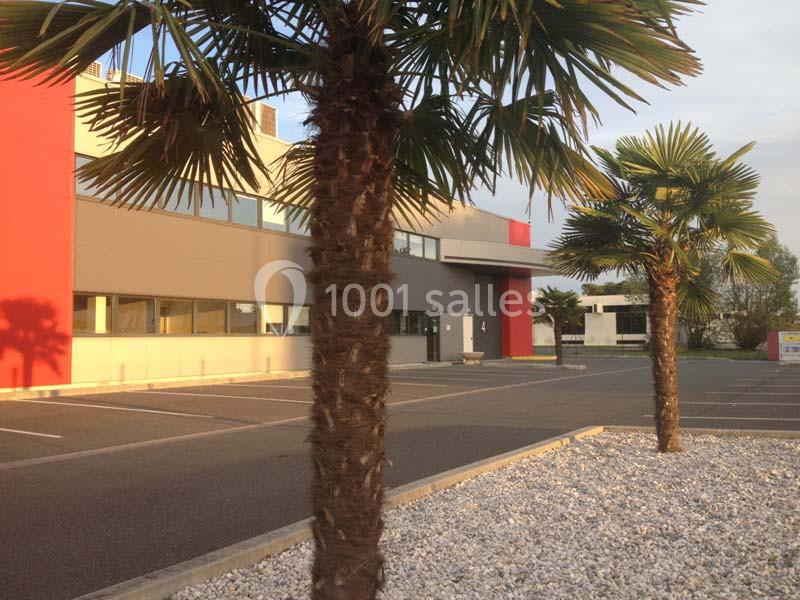 Façade d'un bâtiment moderne avec des palmiers et un parking vide au premier plan.
