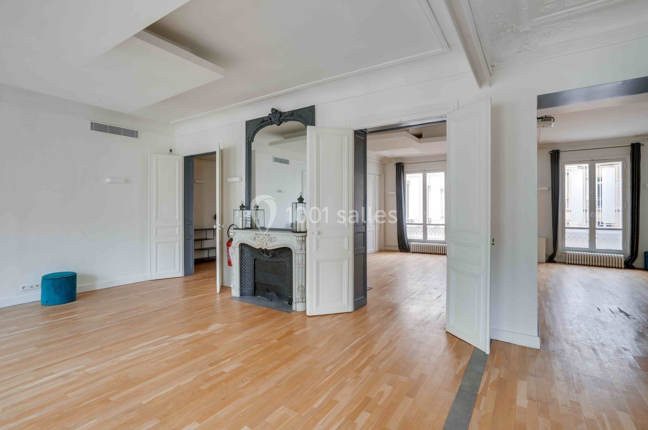 Intérieur lumineux d'un appartement vide avec parquet, cheminée décorative et grandes portes ouvertes sur une autre pièce.