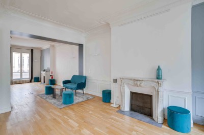 Miniature L’Appart Lafayette – grande salle lumineuse pour réception Salon lumineux avec parquet en bois clair, cheminée, fauteuils bleus et moulures au plafond.