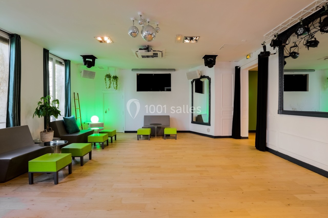 Les Salons Parisiens – appartement de réception près de l'Opéra Garnier Salle lumineuse avec parquet, mobilier moderne vert et gris, éclairage décoratif et scène équipée de projecteurs.