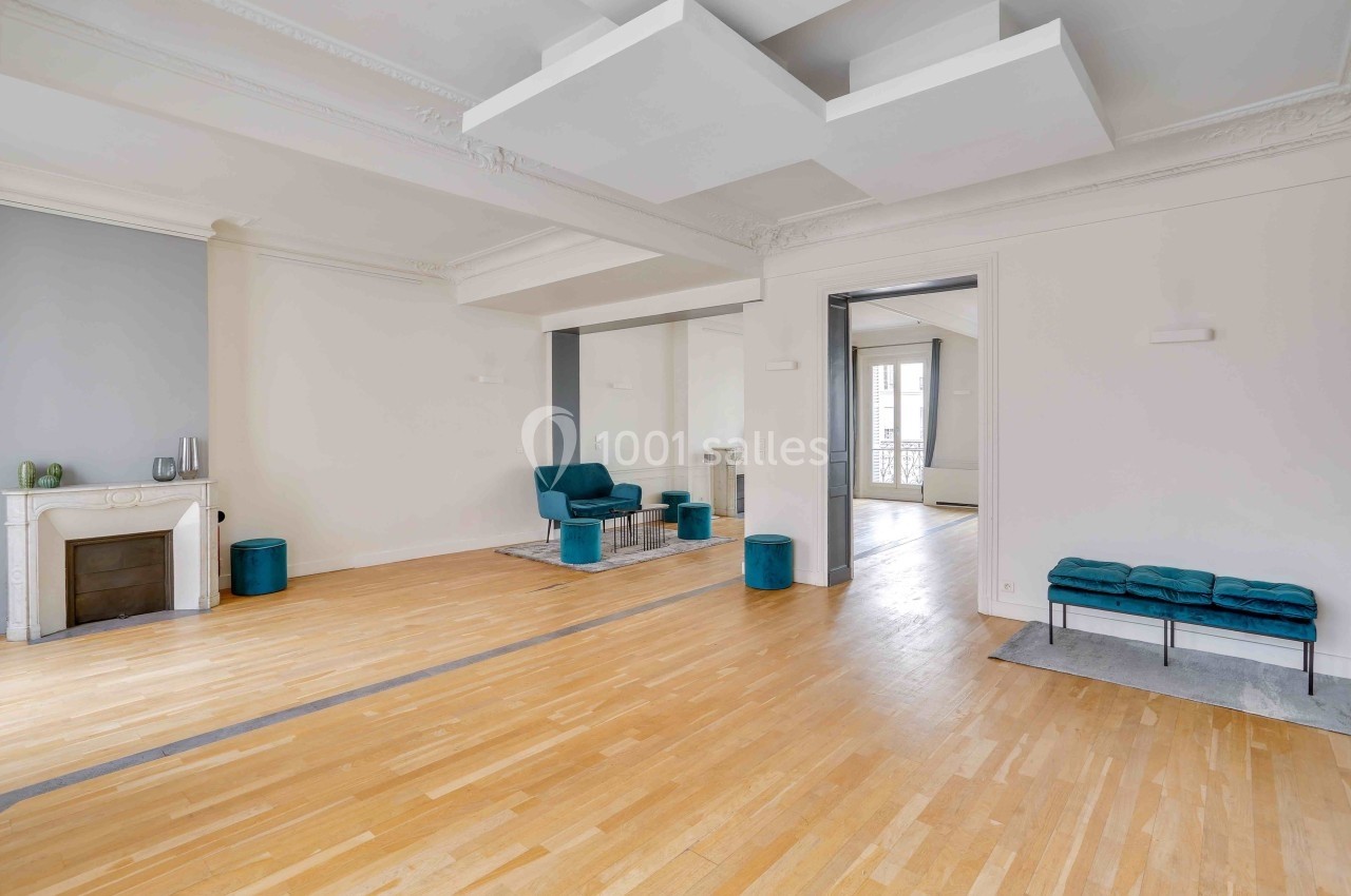 Les Salons Parisiens – appartement de réception rue La Fayette Salon lumineux avec parquet en bois clair, cheminée, fauteuils bleus et moulures au plafond.