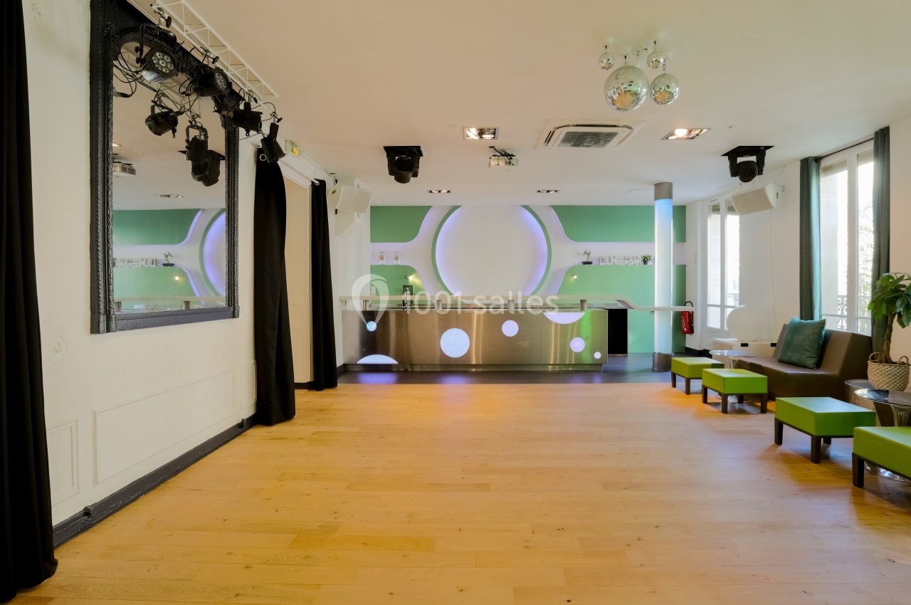 Les Salons Parisiens – réception privée au cœur de Paris Salle lumineuse avec parquet clair, comptoir moderne en métal, murs verts et sièges verts près des fenêtres.