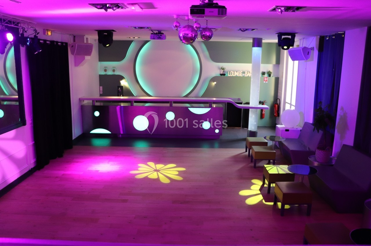 Salon Lafayette – ambiance soirée et anniversaire à Paris Salle de réception moderne avec bar éclairé, parquet en bois clair et jeux de lumières colorées au sol.