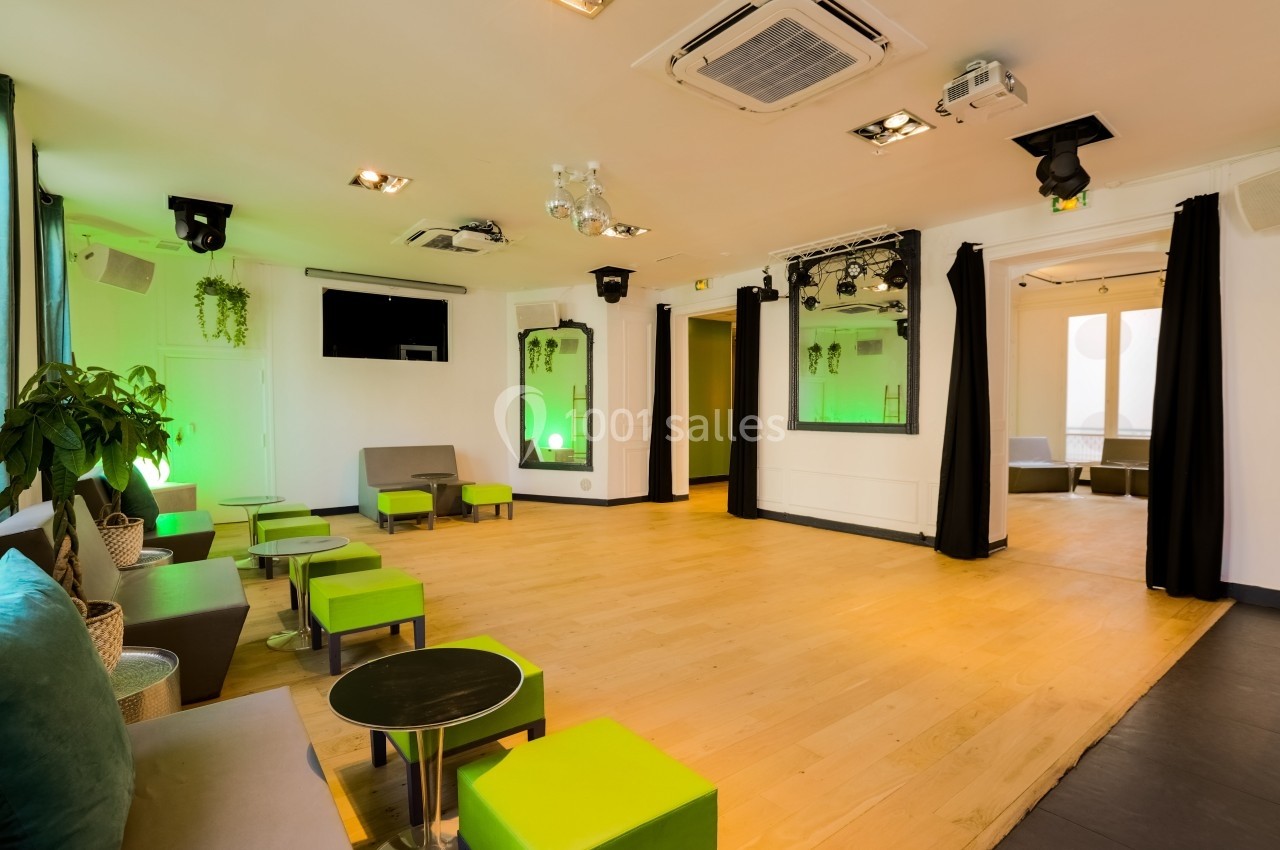 Salon Lafayette – ambiance soirée et anniversaire à Paris Salle lumineuse avec parquet, mobilier moderne vert et gris, éclairage tamisé et plantes décoratives.