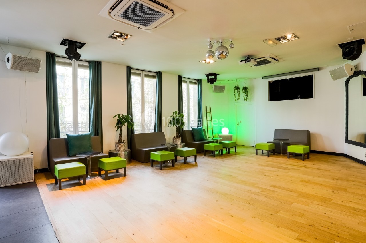 Salon Lafayette – espace cocktail jusqu’à 100 invités Salle lumineuse avec parquet, fauteuils gris et verts, plantes, miroirs, éclairage moderne et fenêtres donnant sur l…