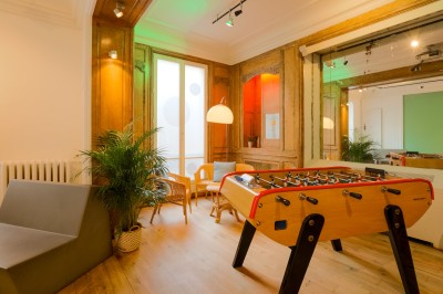 Miniature Salon Lafayette espace détente et babyfoot Salon lumineux avec parquet en bois clair, cheminée, fauteuils bleus et moulures au plafond.