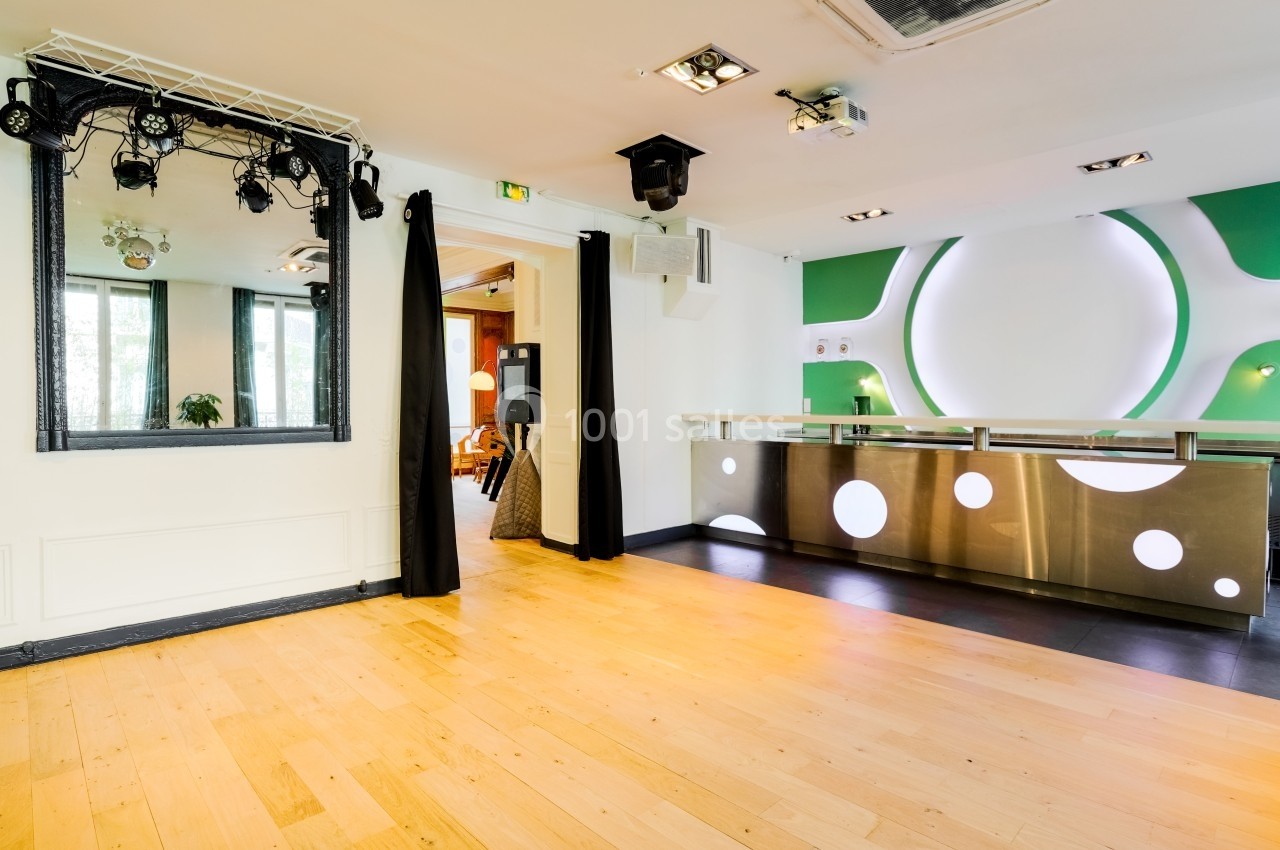 Salon Lafayette – lieu pour fête et réception privée à Paris Salle lumineuse avec parquet, comptoir moderne en métal, miroir encadré noir et éclairages suspendus.