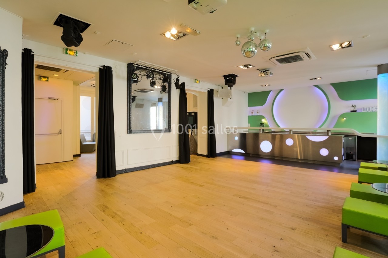 Salon Lafayette – salle de réception jusqu'à 100 personnes à Paris Salle lumineuse avec parquet en bois clair, comptoir moderne et sièges verts, éclairage intégré au plafond.