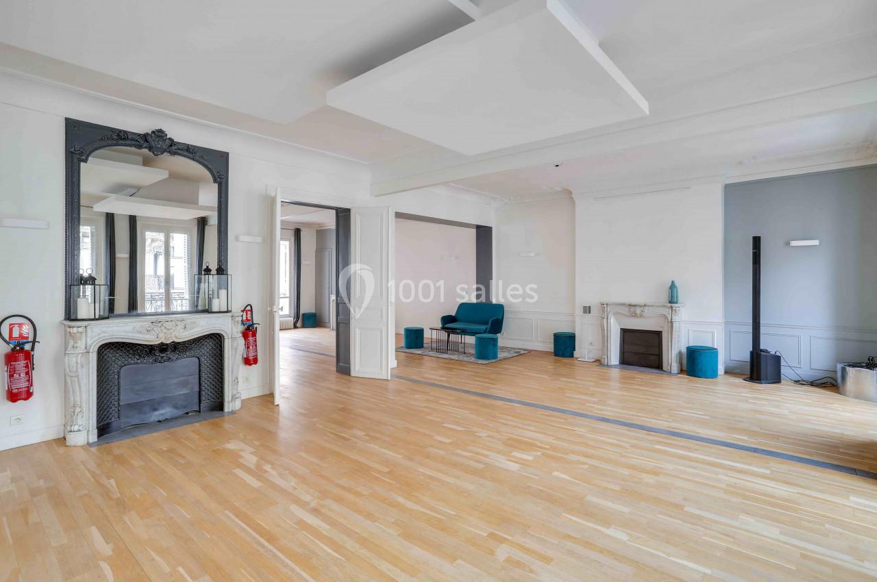 Salle lumineuse avec parquet en bois clair, deux cheminées, un grand miroir et des murs blancs et gris.