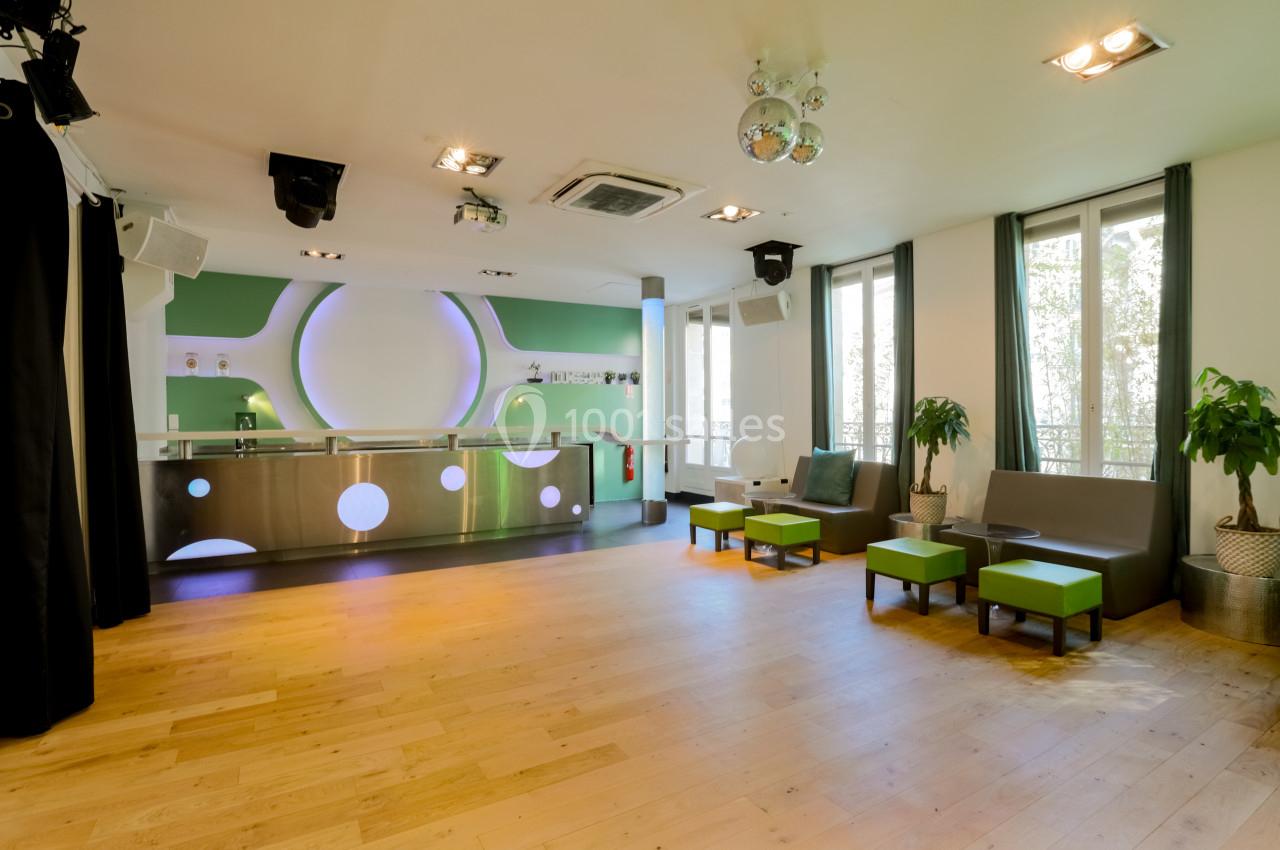 Salle lumineuse avec parquet en bois clair, mobilier vert et blanc, comptoir moderne et grandes fenêtres.