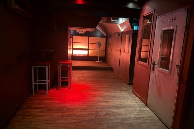 Miniature Location salle Lyon 1 (Rhône) - Le Temps des Copains #6 Salle sombre avec un éclairage rouge au fond, tabourets alignés à gauche et un comptoir à droite.