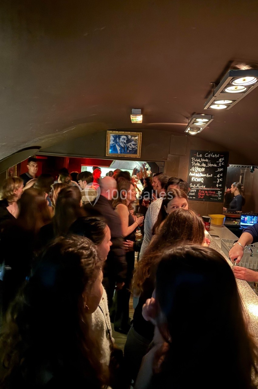 Groupe de personnes discutant et commandant des boissons dans un bar animé avec une ambiance tamisée.