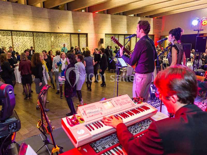 Un groupe de musiciens joue sur scène pendant qu'un public danse dans une salle éclairée et animée.