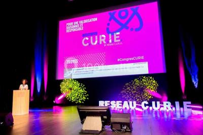 Un groupe de musiciens joue sur scène pendant qu'un public danse dans une salle éclairée et animée.