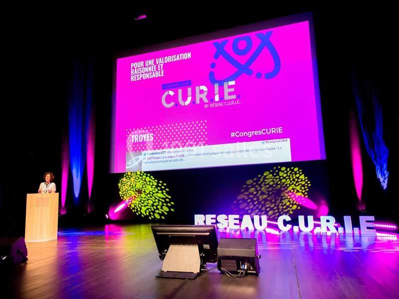Une conférencière sur scène devant un écran projetant une présentation lors d'un événement à Troyes.