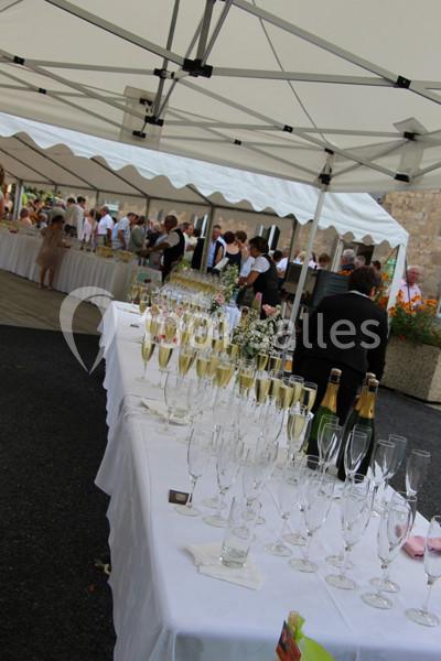 Tables dressées sous une tente avec des verres à champagne et des bouteilles, lors d'un événement en extérieur.