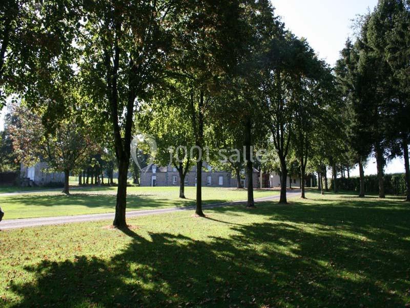 Allée bordée d'arbres dans un parc verdoyant avec des bâtiments en pierre visibles en arrière-plan.