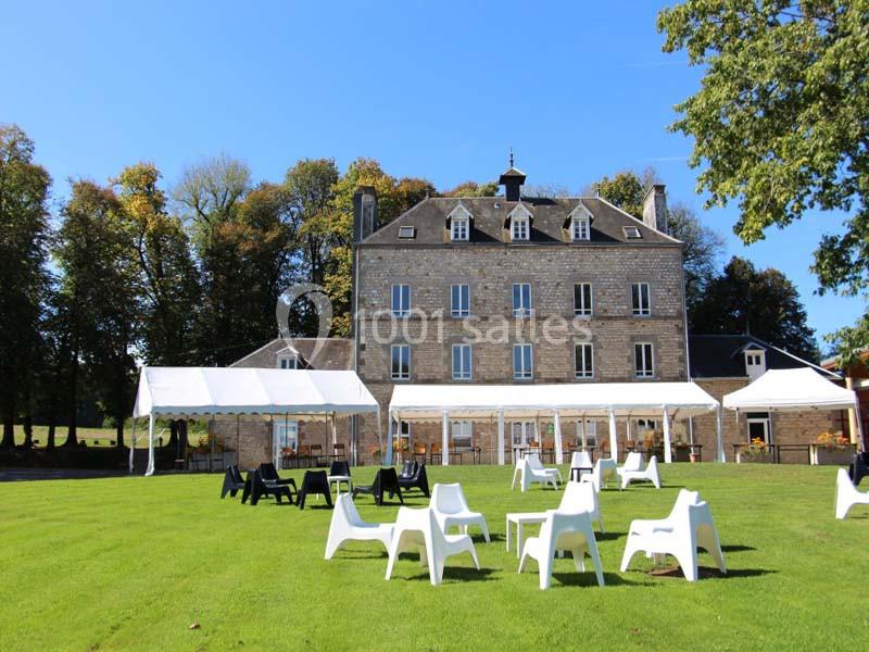 Façade d'un bâtiment en pierre avec des tentes blanches et des chaises disposées sur une pelouse verte.
