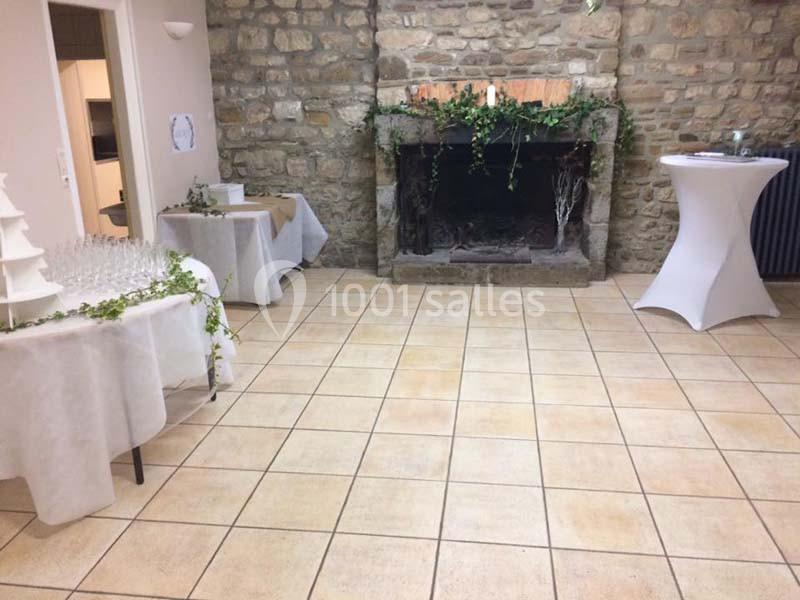 Salle avec cheminée en pierre, tables décorées de nappes blanches et feuillage, sol en carrelage beige.