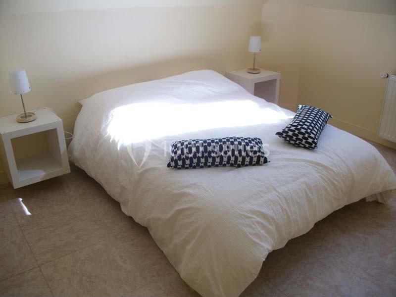 Lit double avec housse blanche, deux coussins à motifs noirs et blancs, tables de chevet blanches avec lampes.