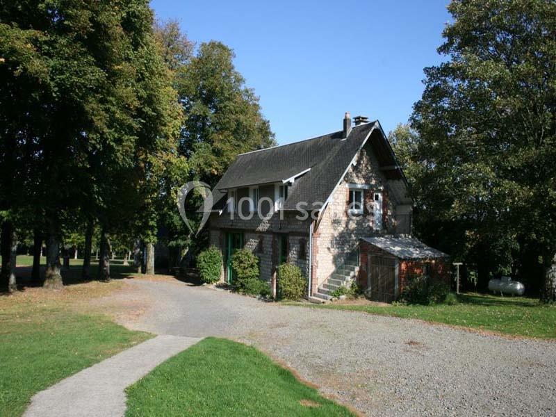 Maison en pierre entourée d'arbres, avec une allée en gravier et une pelouse au premier plan.