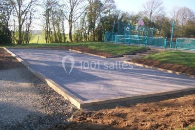 Terrain en cours d'aménagement avec une surface en gravier, entouré de verdure et proche d'un espace de jeux clôturé.