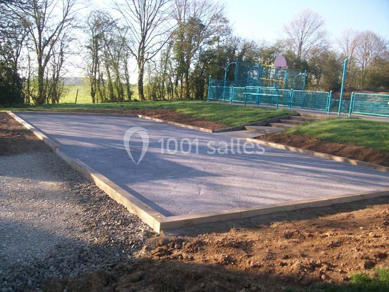 Terrain en cours d'aménagement avec une surface en gravier, entouré de verdure et proche d'un espace de jeux clôturé.