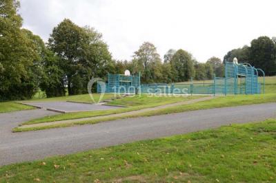 Terrain en cours d'aménagement avec une surface en gravier, entouré de verdure et proche d'un espace de jeux clôturé.