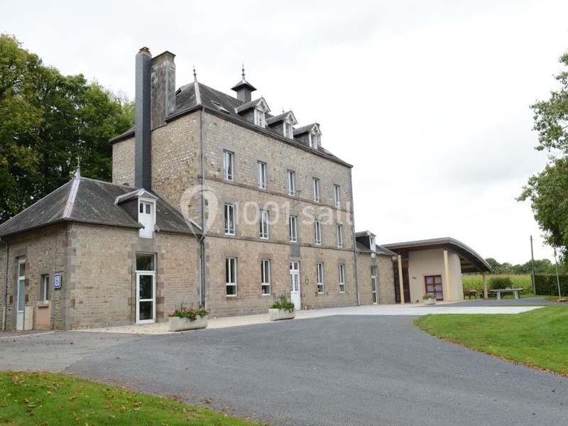 Bâtiment en pierre à plusieurs étages avec toit mansardé, entouré de verdure et d'une allée asphaltée.