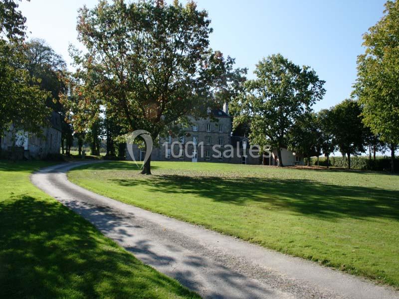 Allée sinueuse bordée de pelouse menant à un bâtiment en pierre entouré d'arbres sous un ciel dégagé.