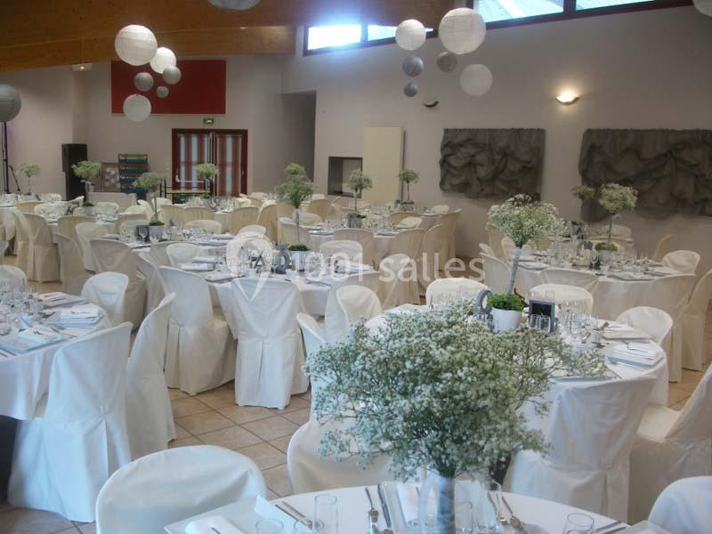 Salle de réception décorée avec des tables rondes, nappes blanches et centres de table fleuris.