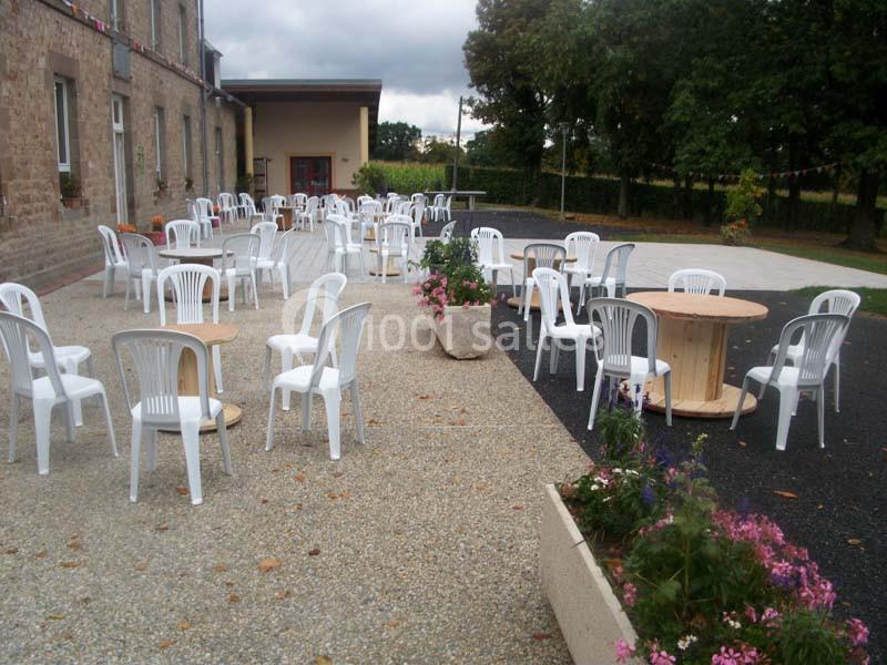 Chaises blanches et tables disposées en extérieur sur une terrasse en gravier près d'un bâtiment en pierre.