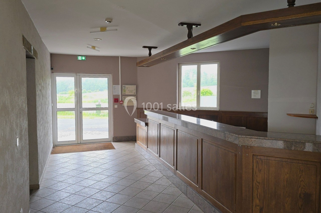 Hall d'entrée avec comptoir en bois, sol carrelé, porte vitrée donnant sur un extérieur verdoyant.