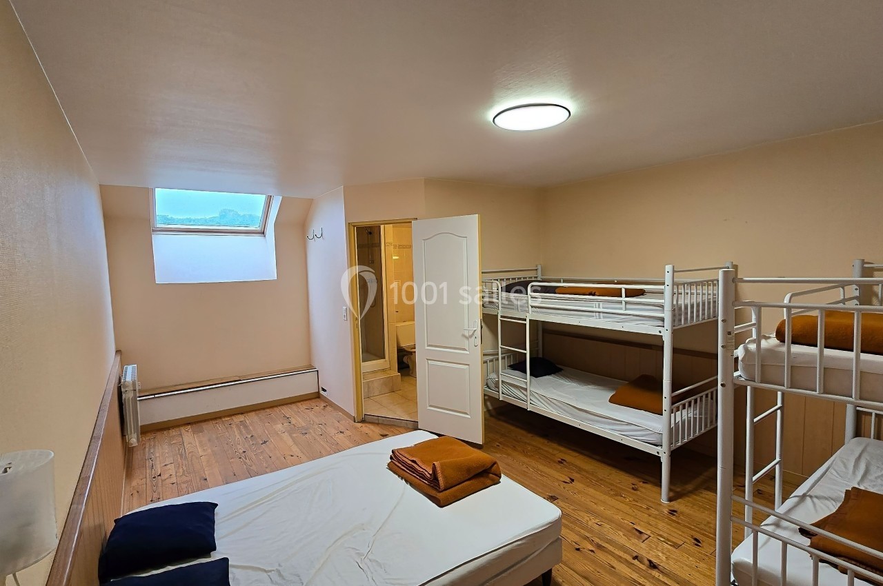Chambre avec lits superposés, un lit simple, parquet au sol, fenêtre en hauteur et salle de bain attenante.