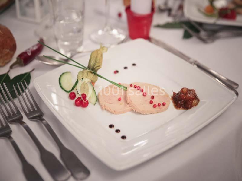 Assiette de foie gras décorée de groseilles, concombre et chutney, servie sur une table dressée élégamment.